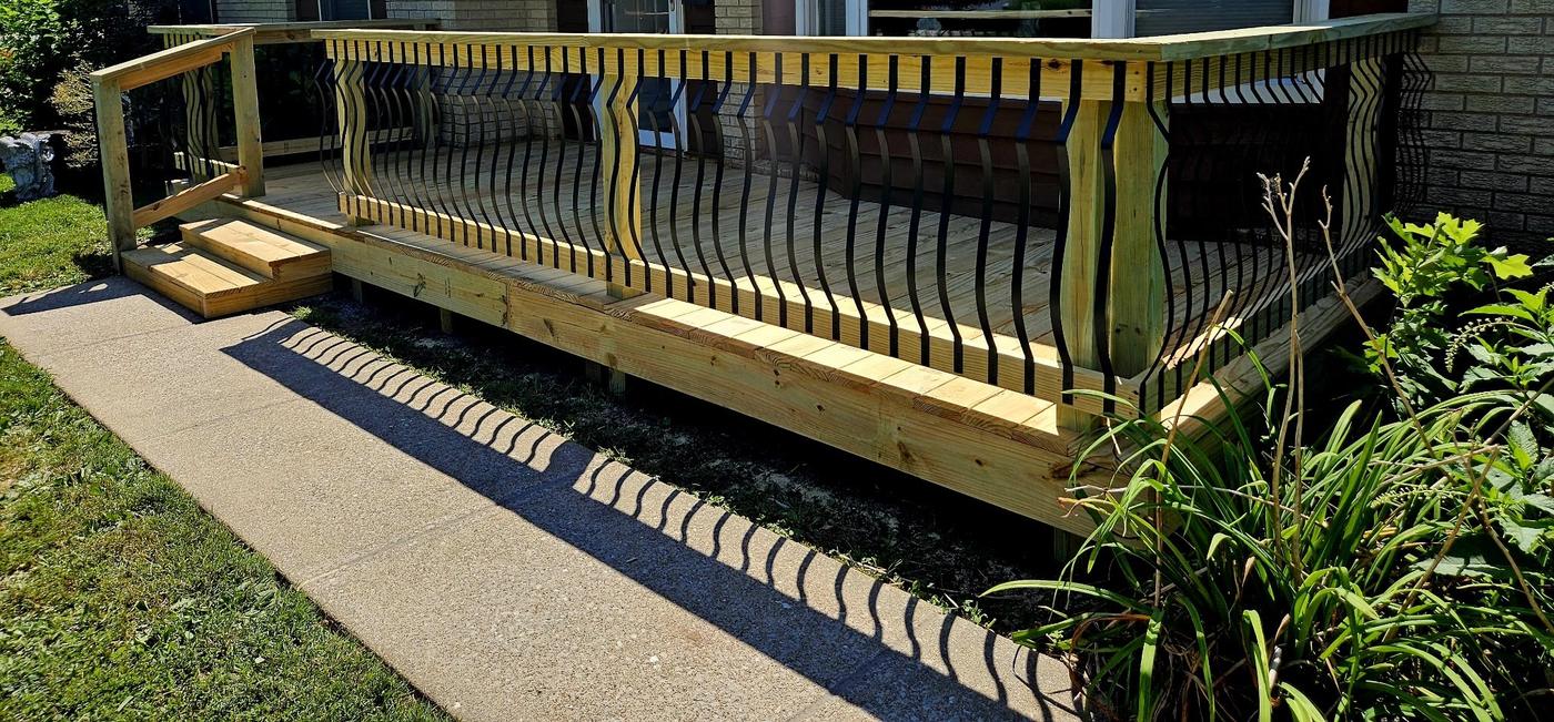 A newly built front deck on a brick house, with curved black metal balusters and timber steps