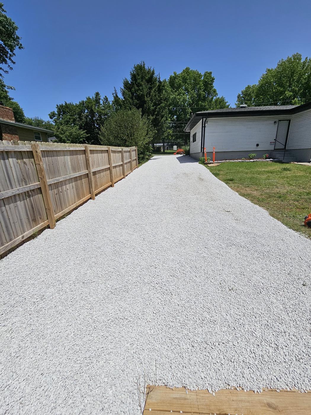 A long white gravel drive running the length of a new timber privacy fence to a garage